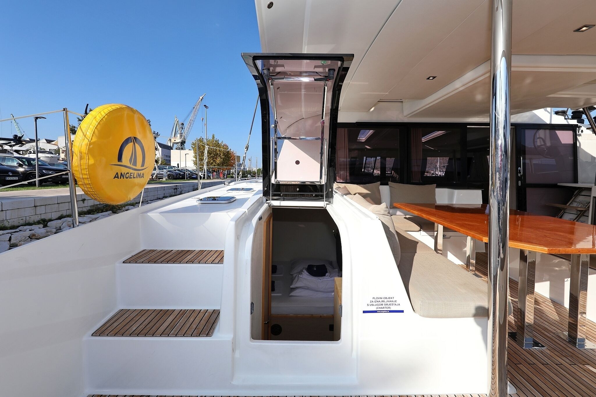 A yacht's deck with a covered seating area, a small enclosed space with a bed, and a yellow inflatable dinghy.