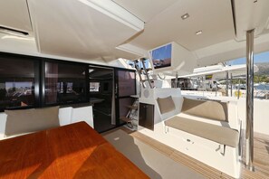 A yacht interior with a dining area, a TV mounted on the ceiling, and a view of the marina. - Sun-kissed Sailing Adventure in Split-Dalmatia, Croatia (Trogir)