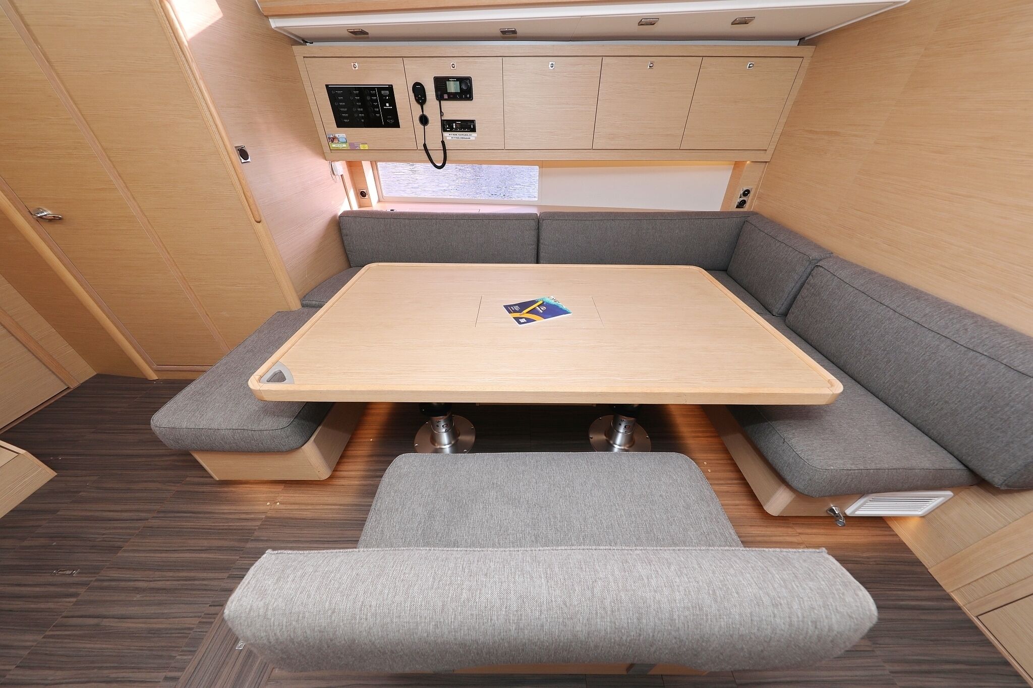 En kompakt autocamper indretning med et centralt bord, grå polstrede sæder og et kontrolpanel over.