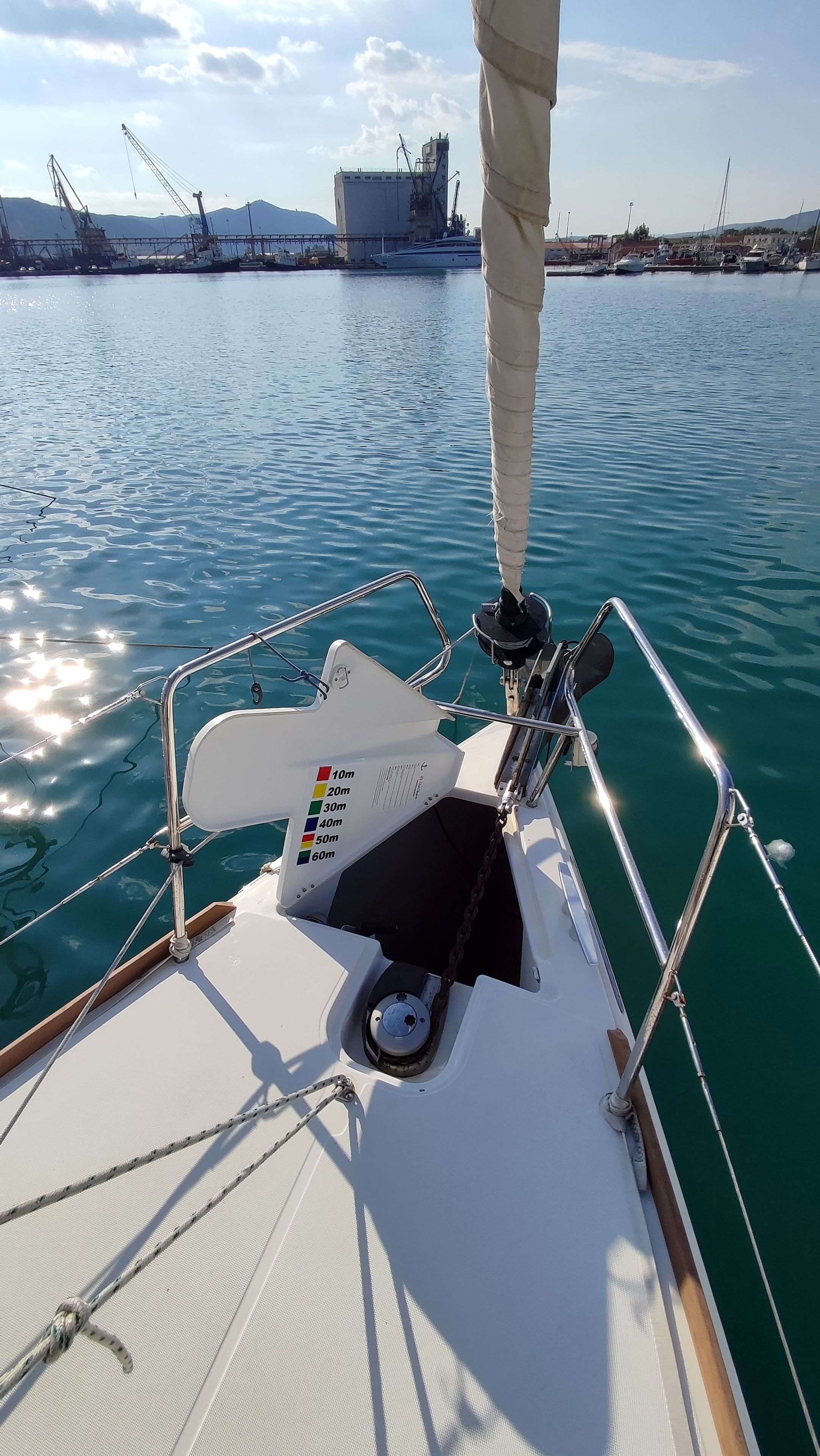 A sailboat's deck with a control panel, ropes, and a view of the water and distant structures.
