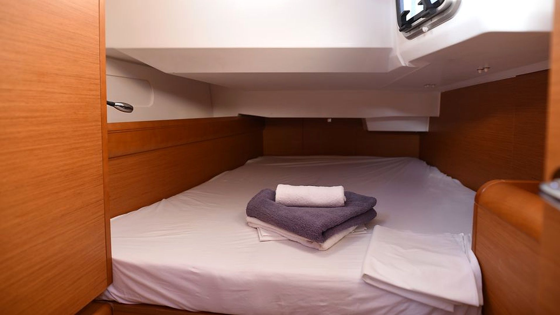 A small, compact room with a single bed, a wooden headboard, and a small overhead shelf.