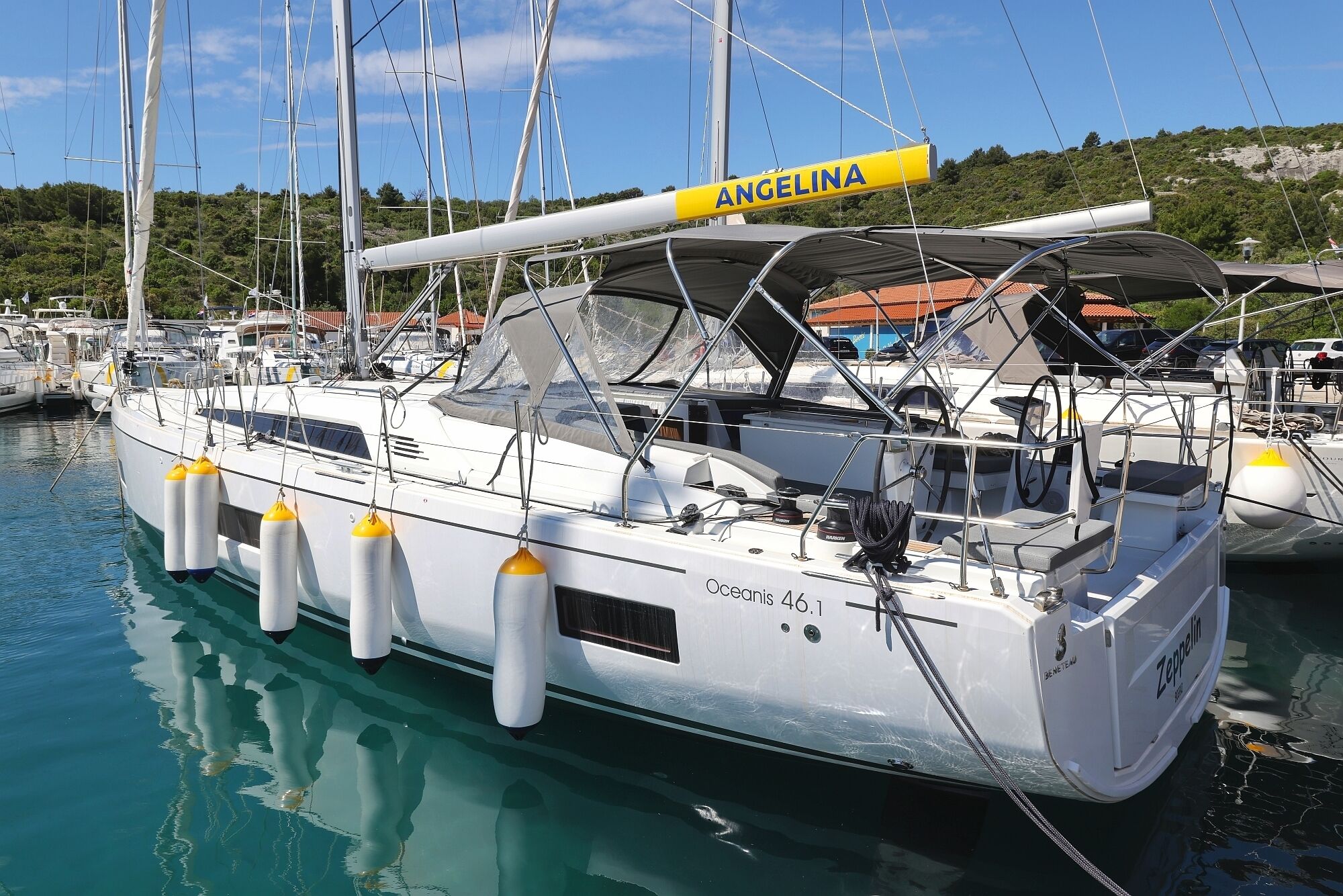 A yacht named 'ANGELINA' docked at a marina with other boats, featuring a covered deck and multiple bollards.