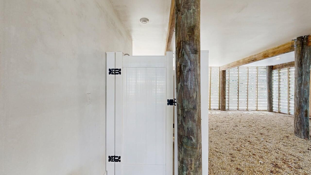 Ein Zimmer mit weißer Tür, Holzbalken und Blick durch große Fenster.