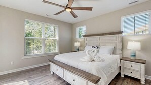 Ein Schlafzimmer mit einem Bett, zwei Nachttischen, einem Deckenventilator und großen Fenstern.