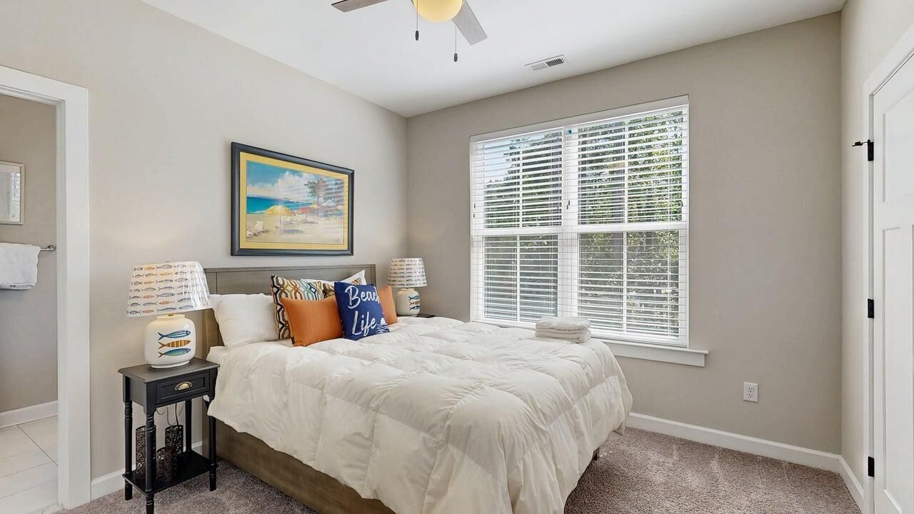 A bedroom with a bed, a window with blinds, a ceiling fan, and a framed picture on the wall.