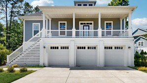 Ein zweistöckiges Haus mit einer Veranda, einer Treppe und zwei Garagen.