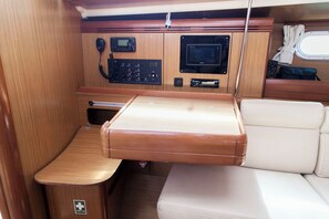 A compact interior with a wooden table, a cushioned bench, a first aid kit, and a mounted radio. - Sun-kissed Sailing Adventure in the Ionian Islands (Preveza)