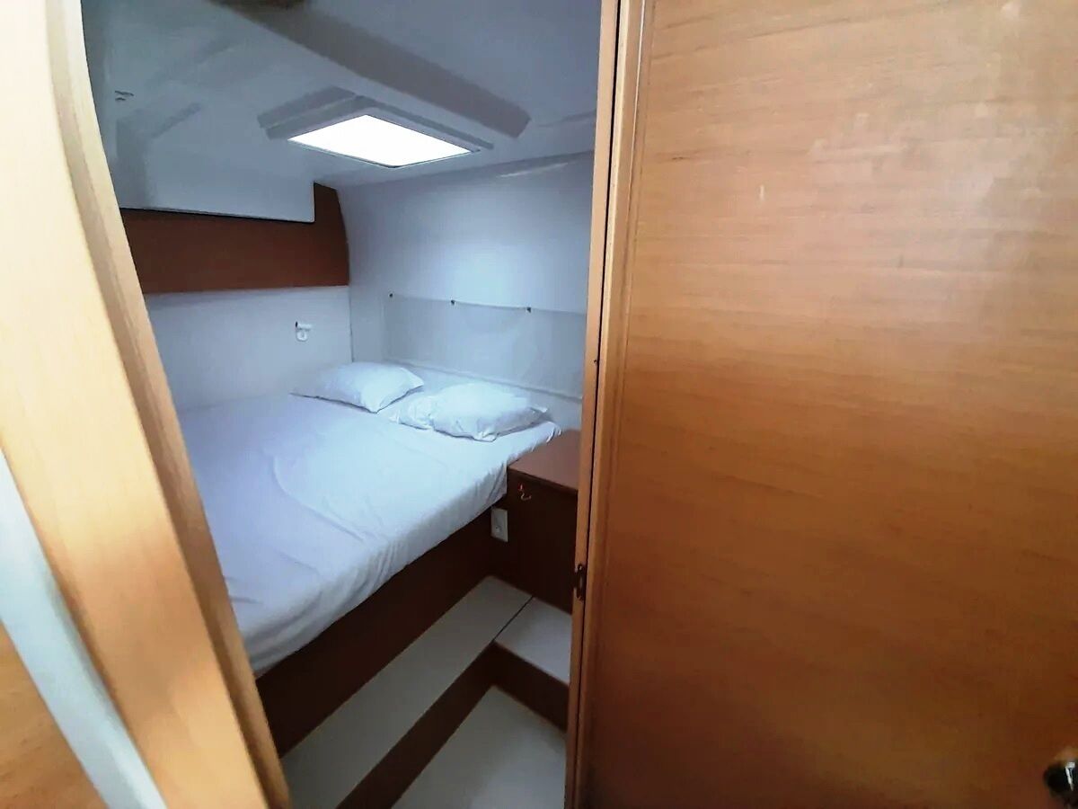 A compact room with a bunk bed, a small bedside table, a ceiling light, and a door.