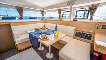 L'intérieur d'un bateau, avec un coin repas, des sièges rembourrés, une table garnie de nourriture et de boissons, et un panneau de commande.