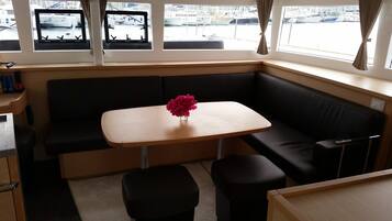 Cabine compacta com sofá, mesa pequena e janela com vista para barcos.