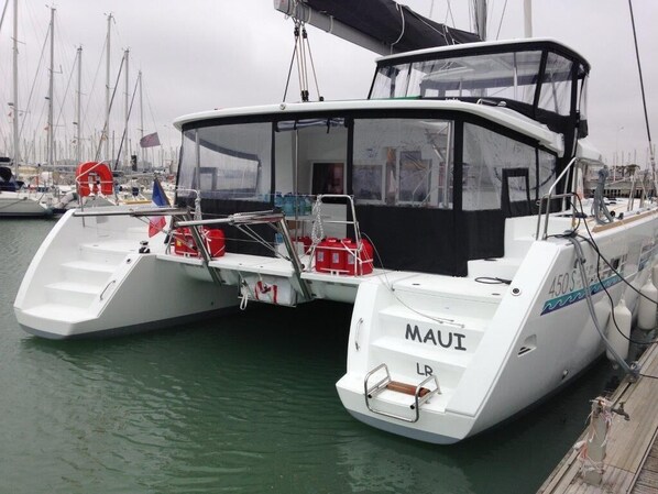 Un barco blanco amarrado en un puerto deportivo, con el nombre 'Maui' en la popa.