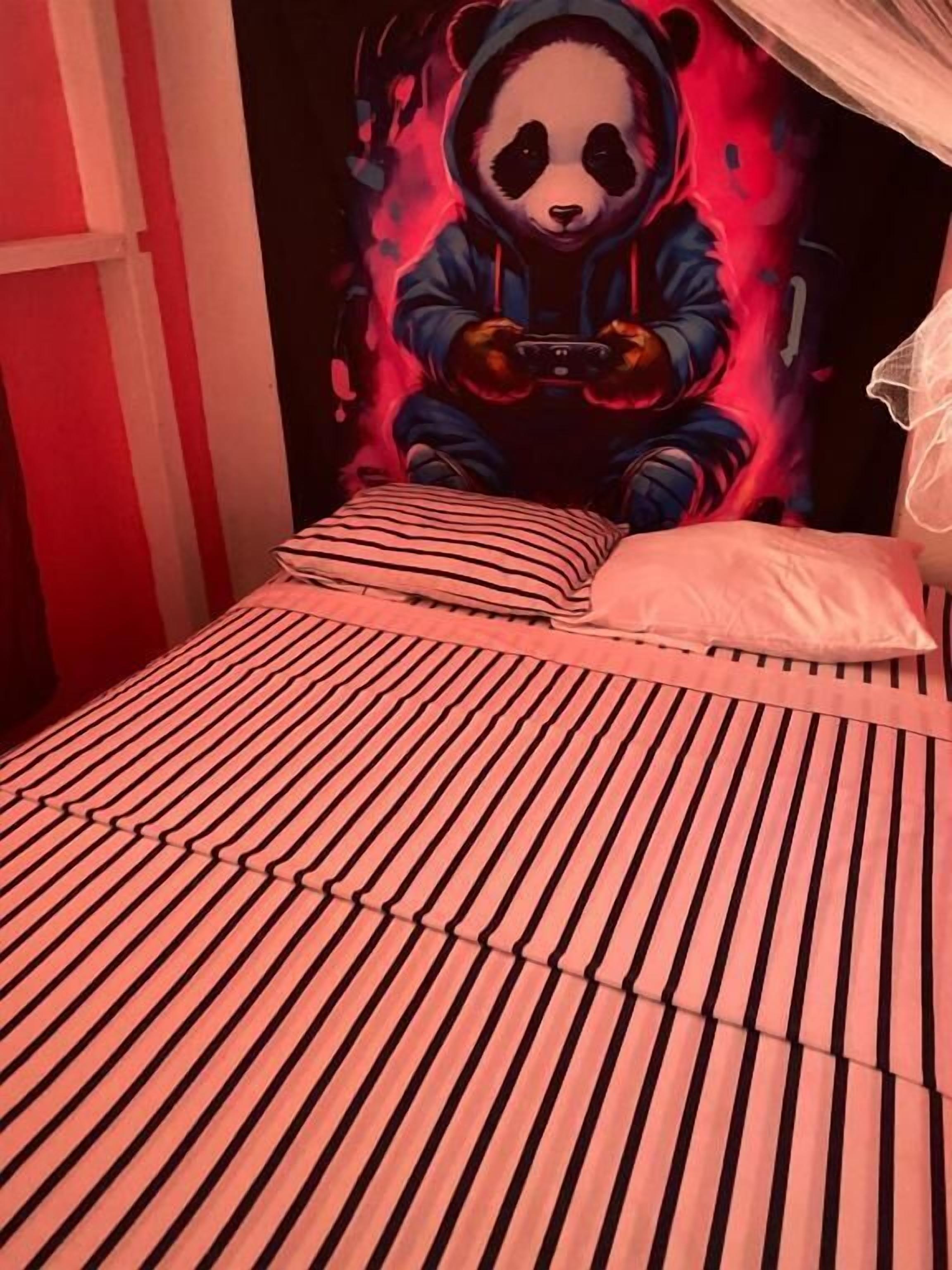 A bed with striped bedding, a canopy, and a wall mural of a panda.
