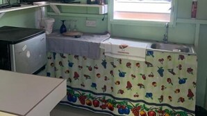 A compact kitchen with a television, sink, and a window with a fruit-patterned curtain. - Minos Haven (Wotten Waven)