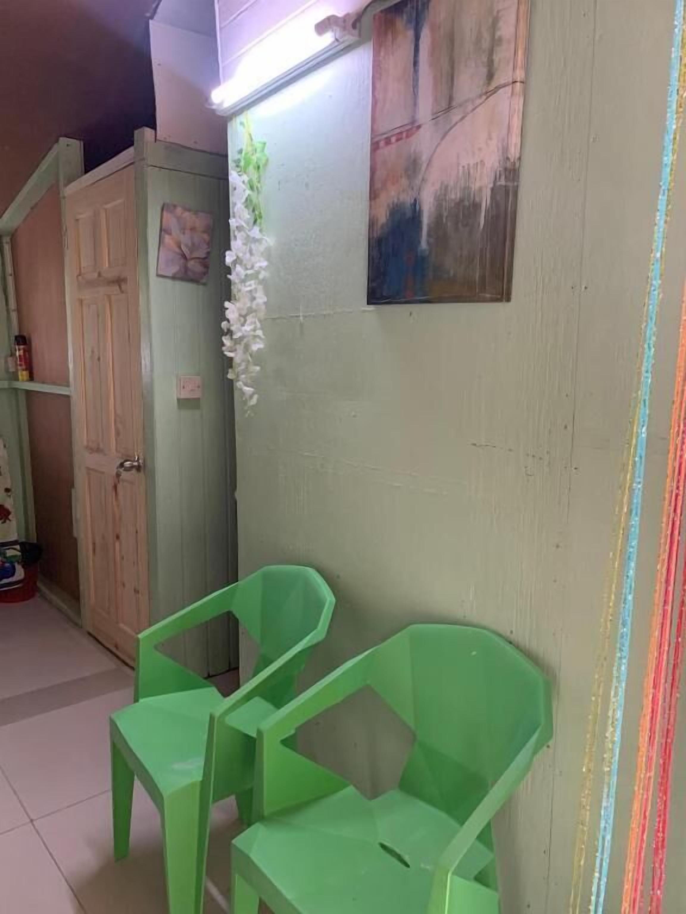 Una habitació amb dues cadires de plàstic verd, un armari, una paret amb un quadre i una làmpada.