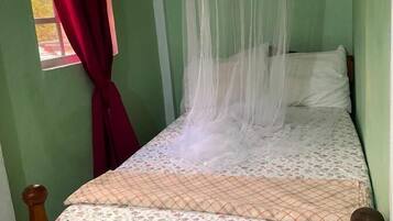 A bed with a wooden headboard, a mosquito net, and a window with a red curtain.