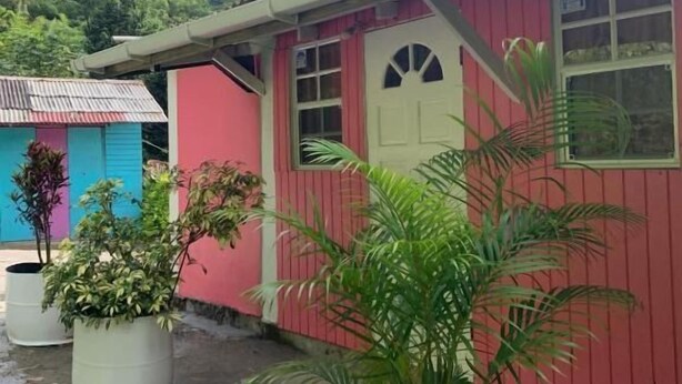 A red building with a white door, potted plants, and a mountain in the background. - Minos Haven (Wotten Waven)