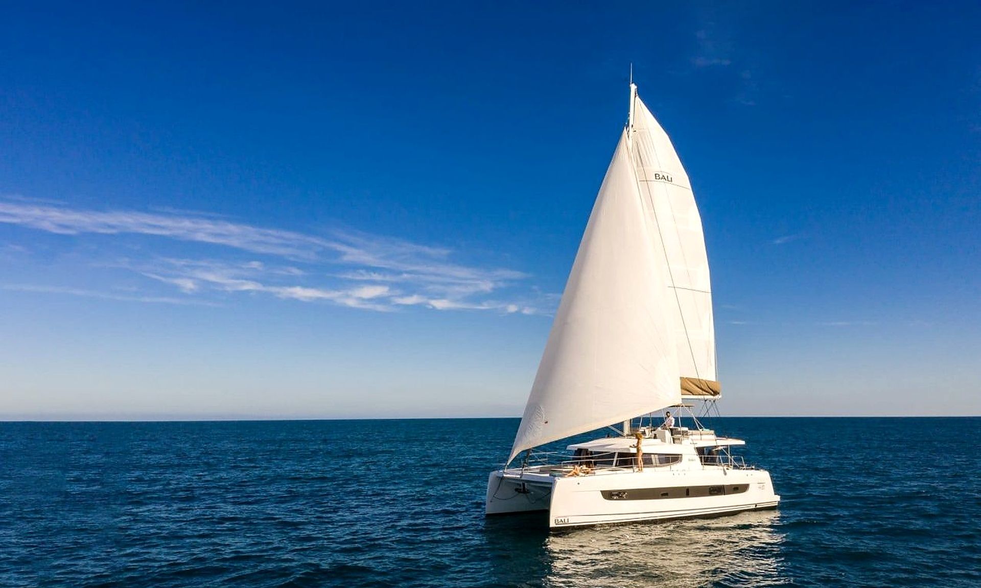 A sailboat with a white sail and the word 'BALI' on its hull, sailing on the ocean.