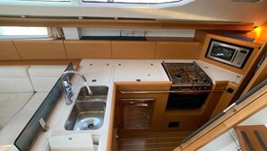 Una cocina pequeña y funcional con lavamanos, estufa y microondas, armarios de madera y una ventana sobre el lavamanos.