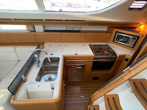 A compact galley with a sink, stove, and microwave, wooden cabinetry, and a window above the sink. - Sun-Kissed Sailing Adventure in the Sporades Islands from Volos, Thessaly (Volos)