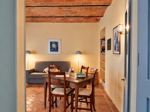 A dining area with a wooden table and chairs, a sofa, and a wall-mounted painting. - "Il Leccio" Apartment in an authentic Tuscan farmhouse with pool (Toscana)