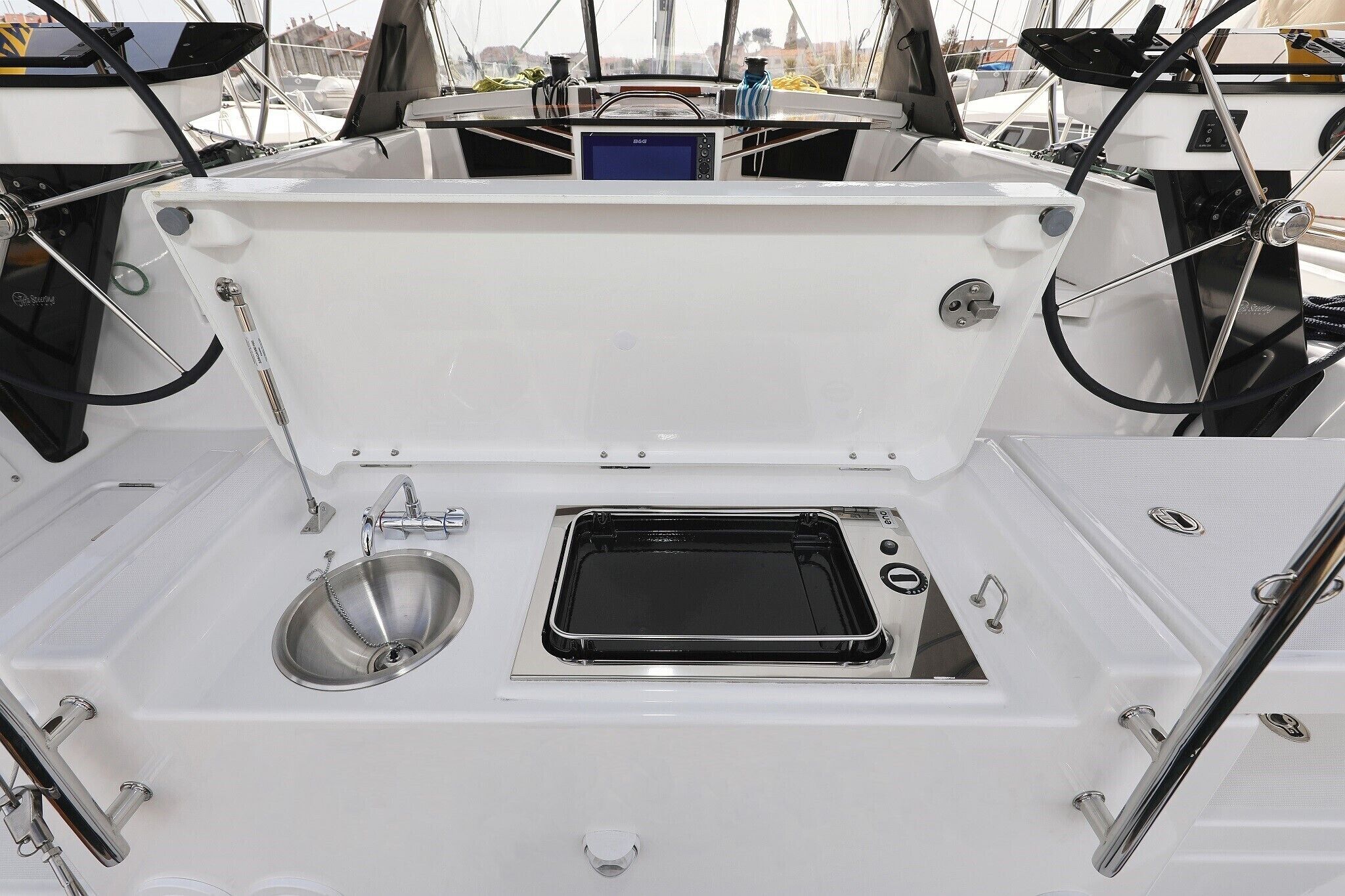 A boat's deck with a steering wheel, a small sink, and a metal tray.