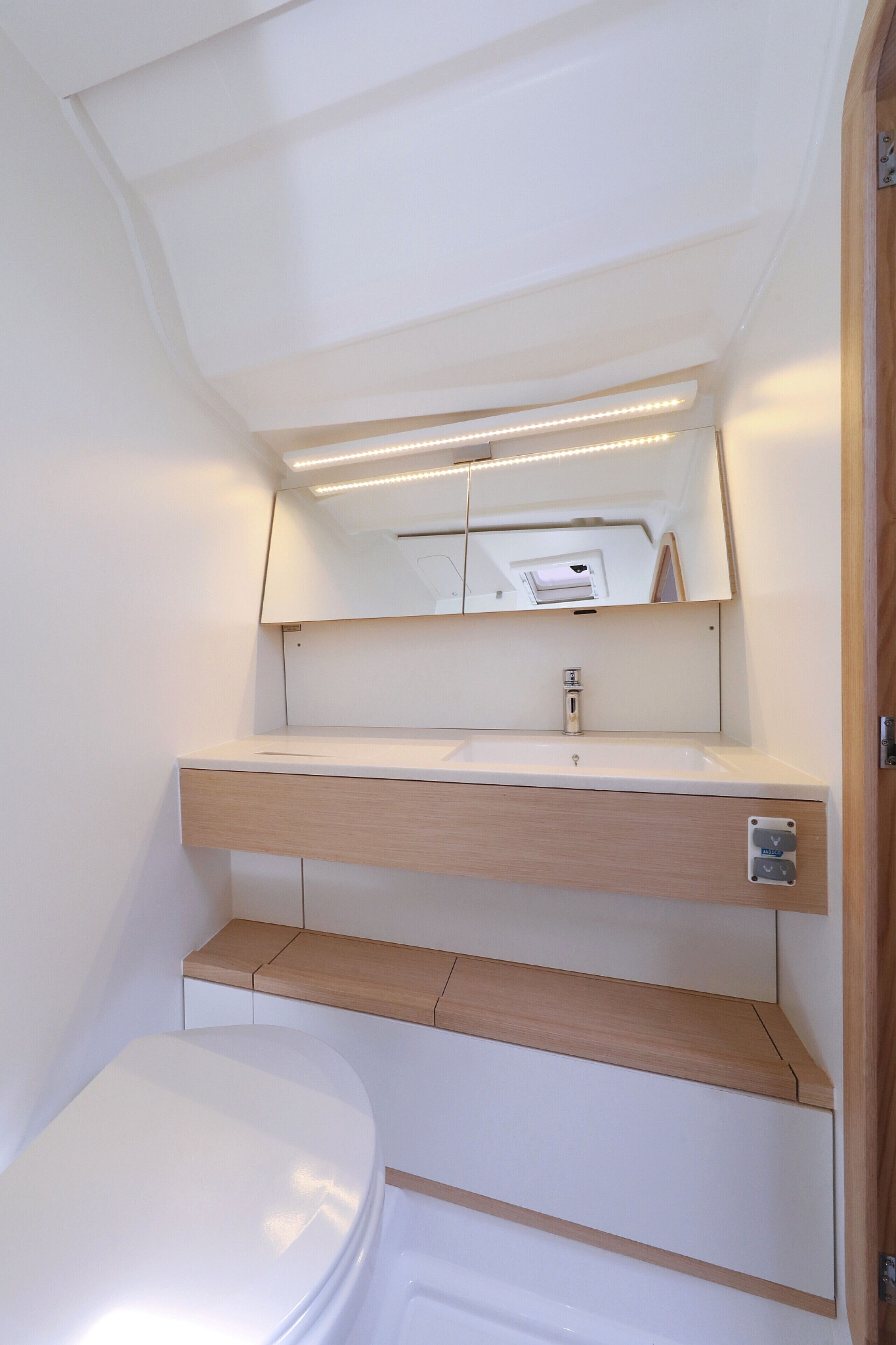 A compact bathroom with a white toilet, a sink with a mirror above it, and a small shelf.