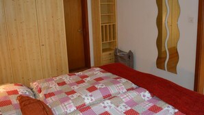 Ein Schlafzimmer mit einem Bett, einem Kleiderschrank, einer eingebauten Regaleinheit und einem Spiegel an der Wand.