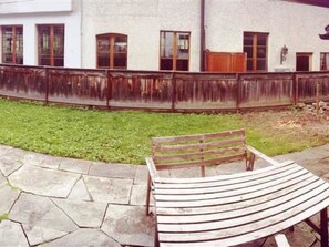 A bench in a courtyard with a stone floor, a white building with windows and a wooden fence in the background. - Oehrli Appartement/Fewo, Dusche oder Bad, WC 4-Bettwohnung by Interhome (Gstaad)
