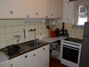 A kitchen with white cabinets, a stainless steel sink, a stove, and various kitchen utensils. - Oehrli Appartement/Fewo, Dusche oder Bad, WC 4-Bettwohnung by Interhome (Gstaad)