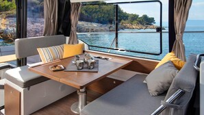 L’intérieur d’un bateau, avec un coin repas, des sièges rembourrés et une vue sur l’eau.