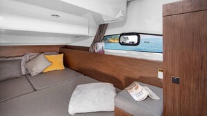 Un intérieur chaleureux avec un canapé, des coussins, une fenêtre donnant sur la mer et une petite table sur laquelle sont posés quelques objets.