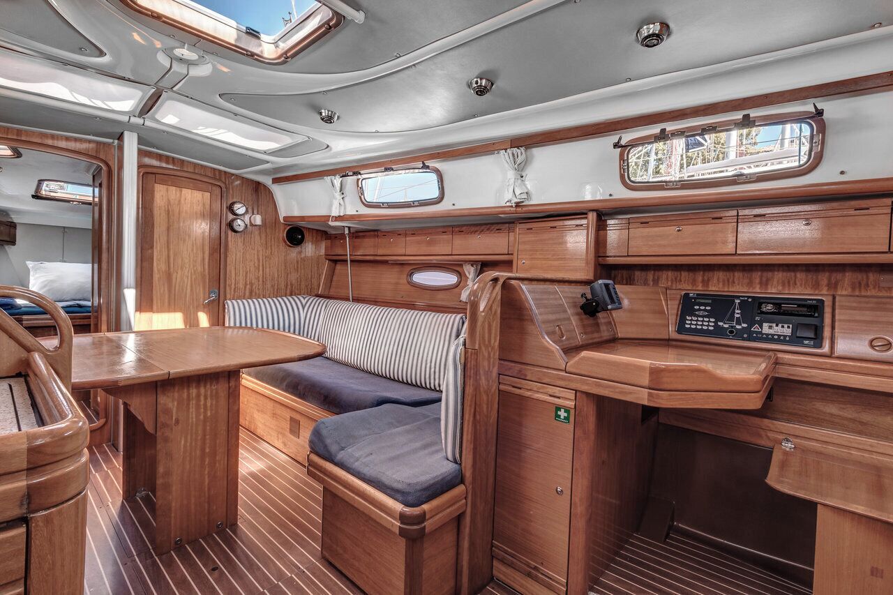 A compact, well-lit interior with a wooden bench, cushioned seating, a control panel, and a window.