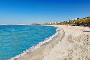 A beach with clear blue water, a sandy shore, and buildings in the background. - Sun-Kissed Sailing Adventure in Islas Sarónicas (Alimos)