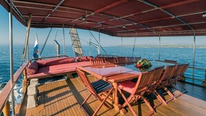 A covered outdoor seating area with a table and chairs, a flag, and a view of the sea. - Sun-Kissed Sailing Adventure in Split, Croatia (Kaštel Gomilica)
