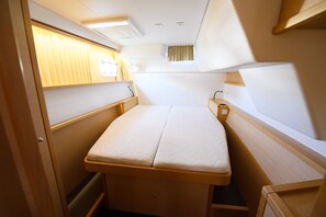 Ein kompakter, gut beleuchteter Innenraum mit einem Einzelbett, einem kleinen Tisch und einem Fenster mit Vorhängen.