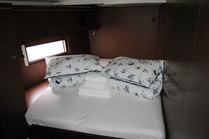 Een klein, compact bed met een raam erboven, een keurig opgemaakt bed met witte lakens en een kussen met een patroon.