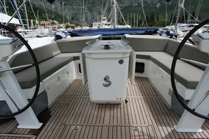 Dek van een boot met een stuurwiel, een bedieningspaneel in het midden en een uitzicht op de jachthaven op de achtergrond.