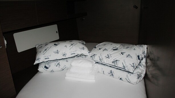 Una cama con ropa de cama y almohadas de diseño náutico, una toalla blanca doblada y un cabecero de madera.