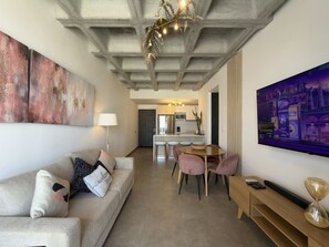 Ein stilvolles Wohnzimmer mit einer Couch, einem Esstisch mit Stühlen, einem Fernseher und Kunstwerken an den Wänden.