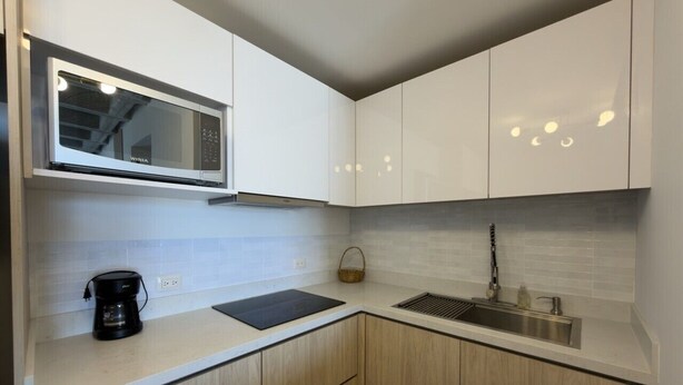 Een moderne keuken met witte kastjes, een ingebouwde magnetron, een koffiezetapparaat en een spoelbak.