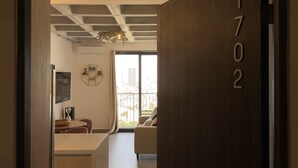 Een modern interieur met een houten deur waarop '1702' staat, een eethoek met tafel en stoelen, en een uitzicht door een groot raam.