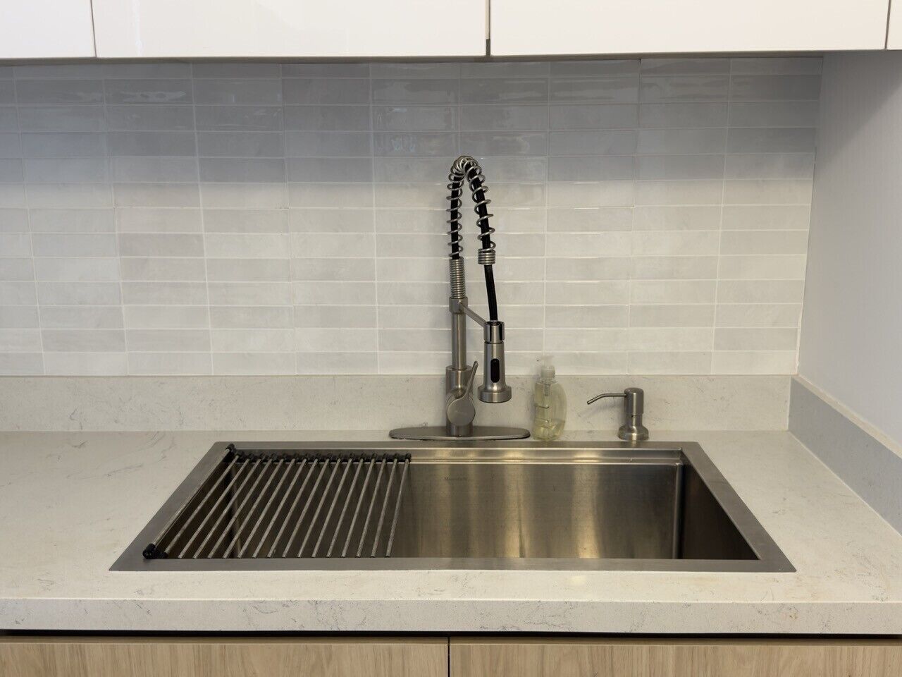 A kitchen with a stainless steel sink, a modern faucet, and a tiled backsplash.