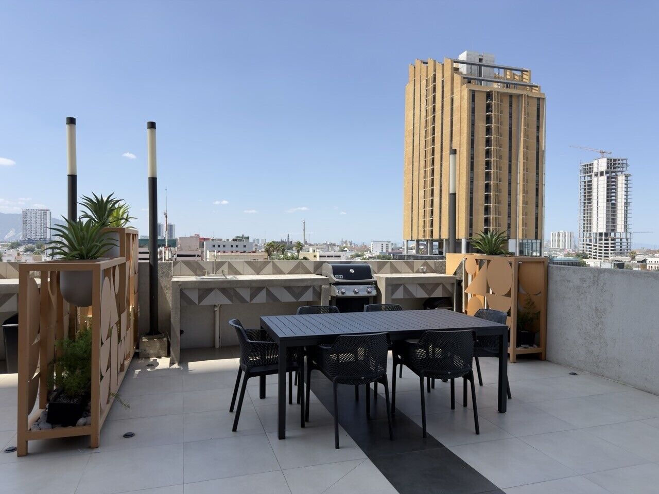 A rooftop terrace with a grill, dining table, chairs, and potted plants.