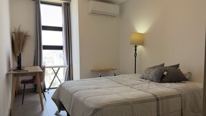 Een slaapkamer met een bed, bureau, stoel, lamp en een airconditioning.