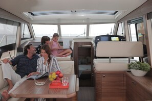 A boat interior with a dining area, a small kitchen, and a seating area with a child. - Sun-Kissed Sailing Adventure in Istria, Croatia (Pula)