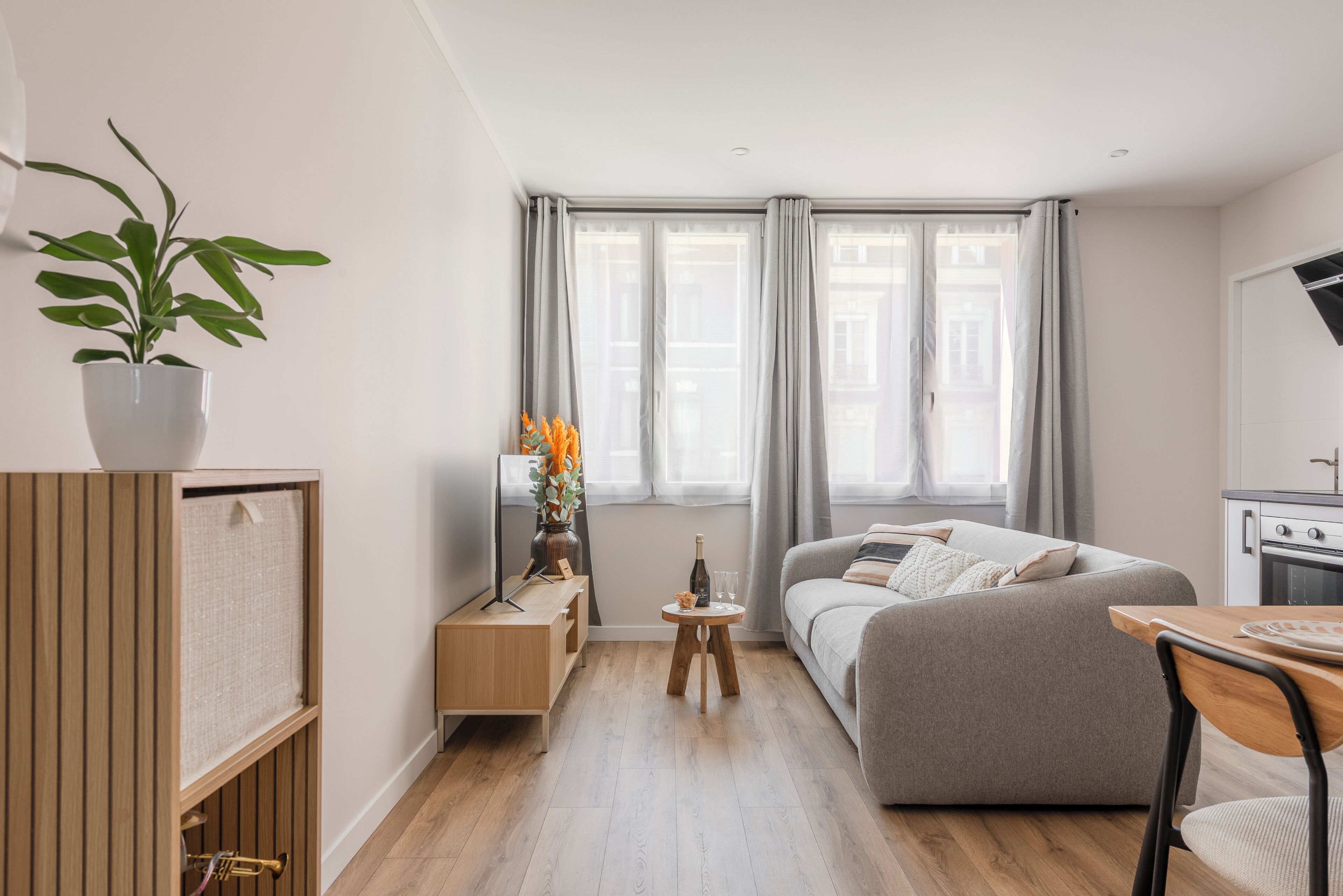 Een moderne woonkamer met een bank, een bijzettafeltje, een plant in pot en uitzicht op de stad door grote ramen.