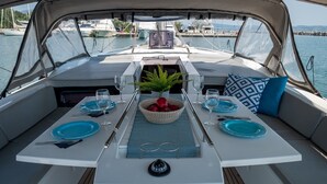 L’espace repas d’un bateau, avec une table dressée pour deux personnes, une plante décorative et une vue sur le port de plaisance.