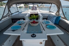 A boat's dining area with a table set for two, a decorative plant, and a view of the marina. - Sun-Kissed Sailing Adventure in the Ionian Islands, Lefkada (Lefkada)