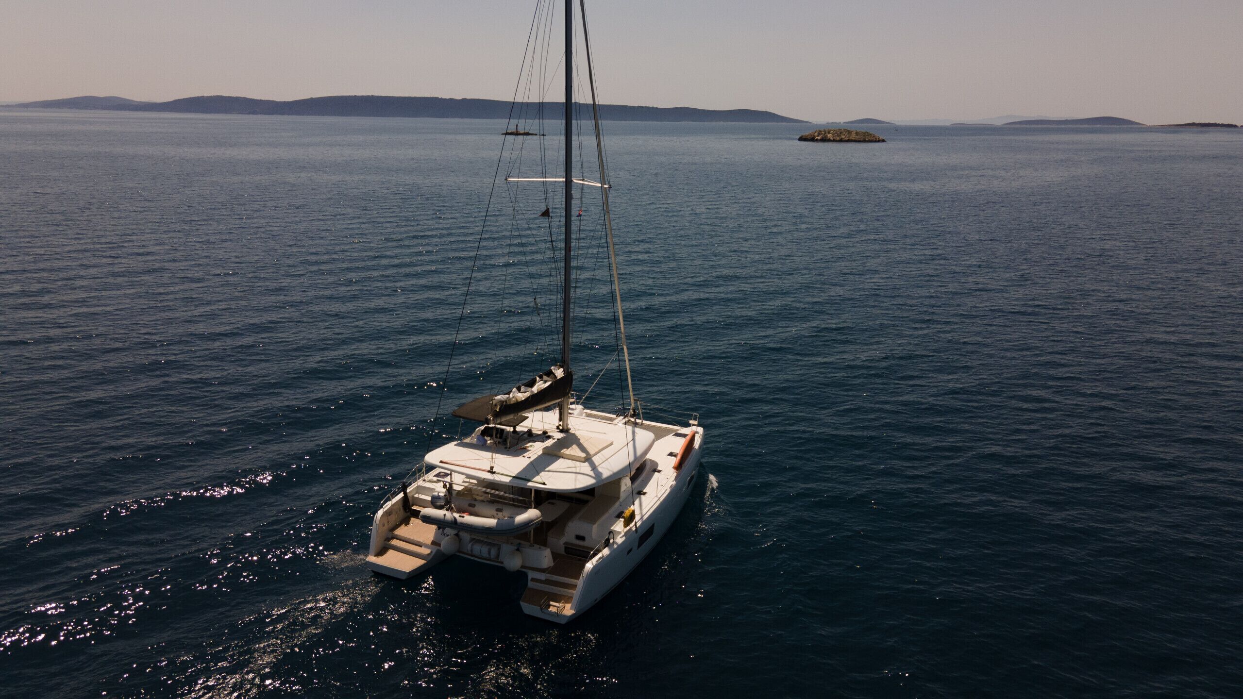A sailboat on calm waters with a distant island and a clear sky.