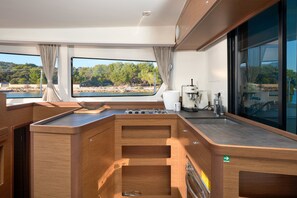 A modern kitchen with a view of a lake, wooden cabinets, and a built-in stove. - Sun-kissed Sailing Adventure in Split-Dalmatia, Croatia (Trogir)